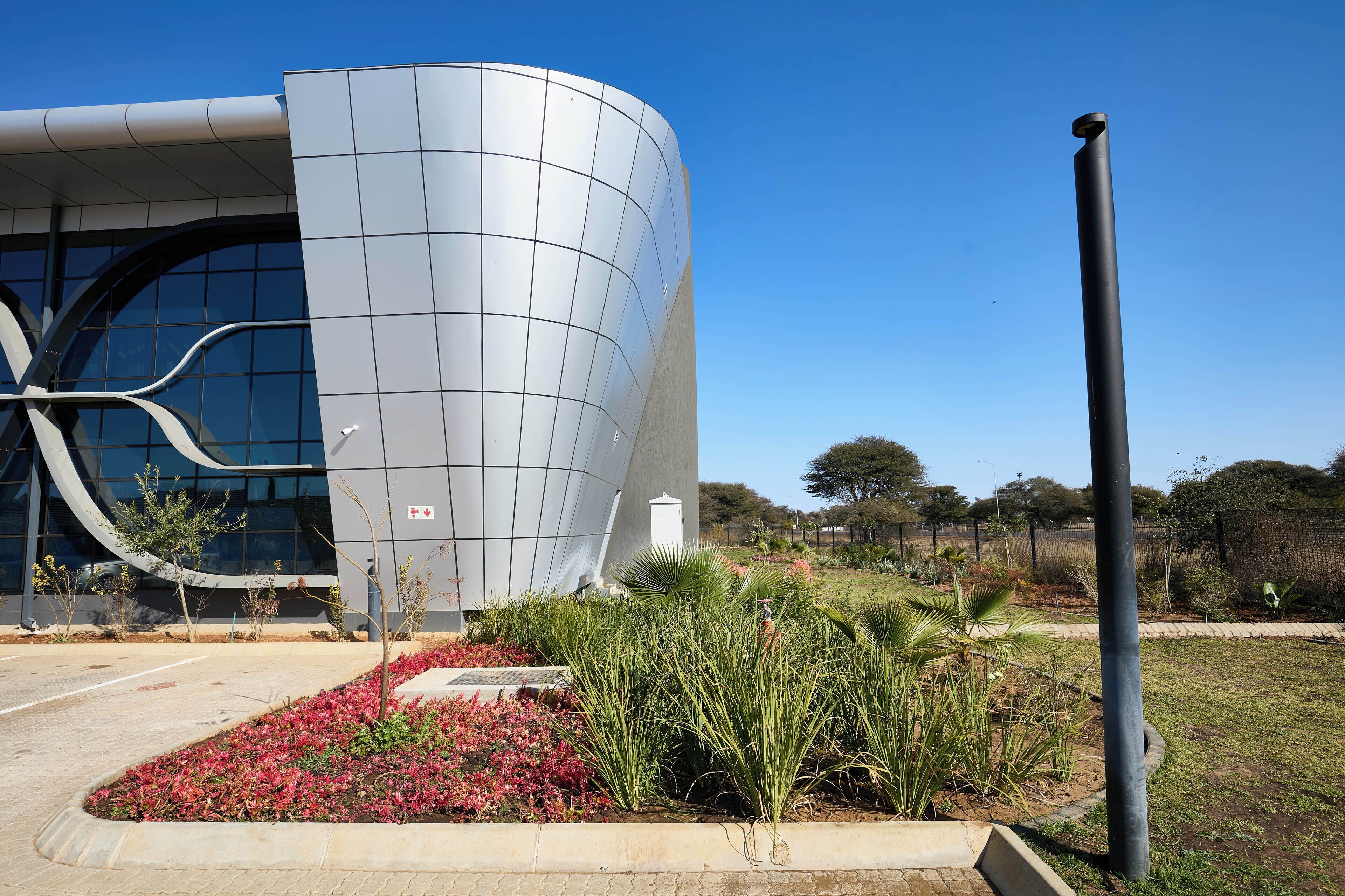 A modern building with a curved facade and a landscaped garden with red flowers and green plants.