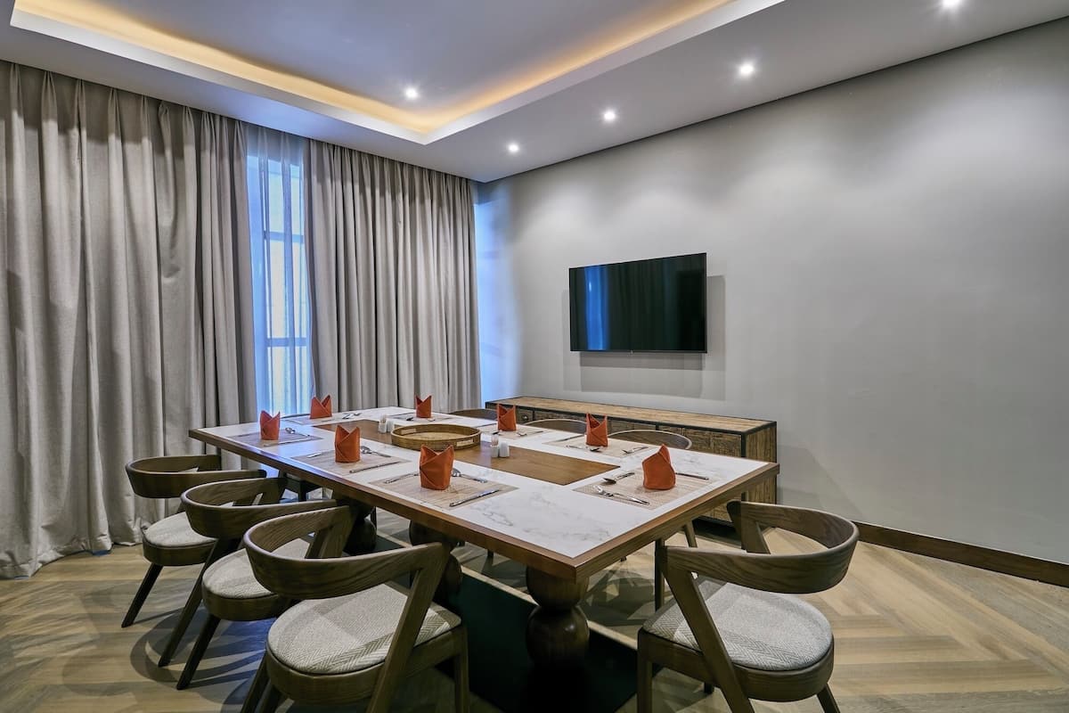 Una sala de conferencias con una mesa larga, sillas, un televisor de pantalla plana y un amplio ventanal con cortinas.