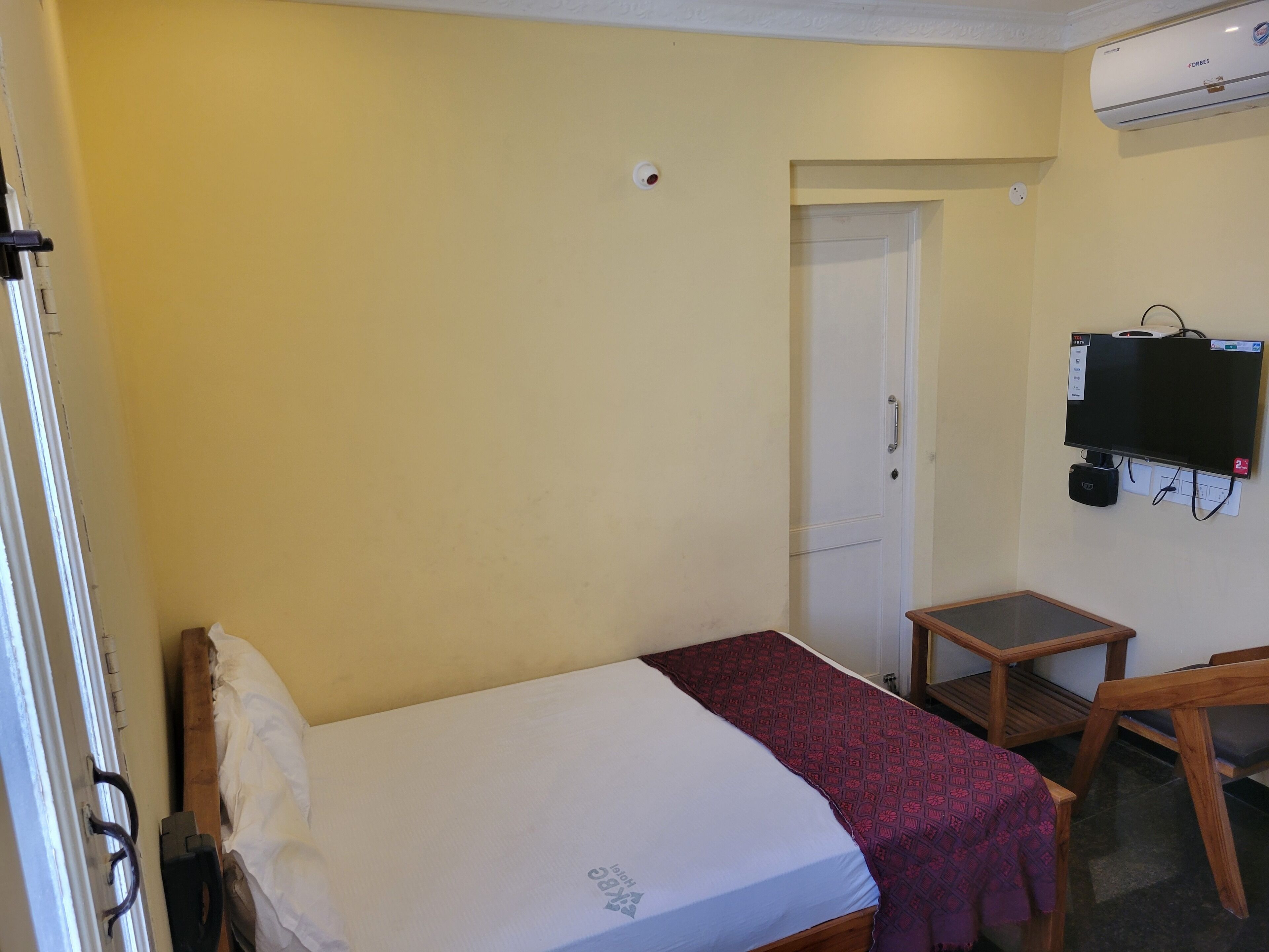 Una habitación pequeña con una cama individual, mesita de noche y un televisor montado en la pared.