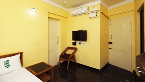Una habitación de hotel con cama, una silla de madera, televisor, equipo de aire acondicionado y una puerta.
