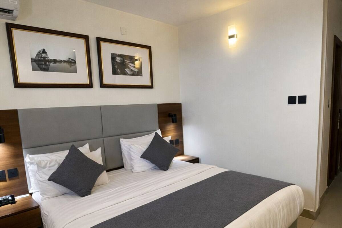 Ein modernes Hotelzimmer mit einem großen Bett, zwei Nachttischen, einer Wandleuchte und zwei gerahmten Bildern.