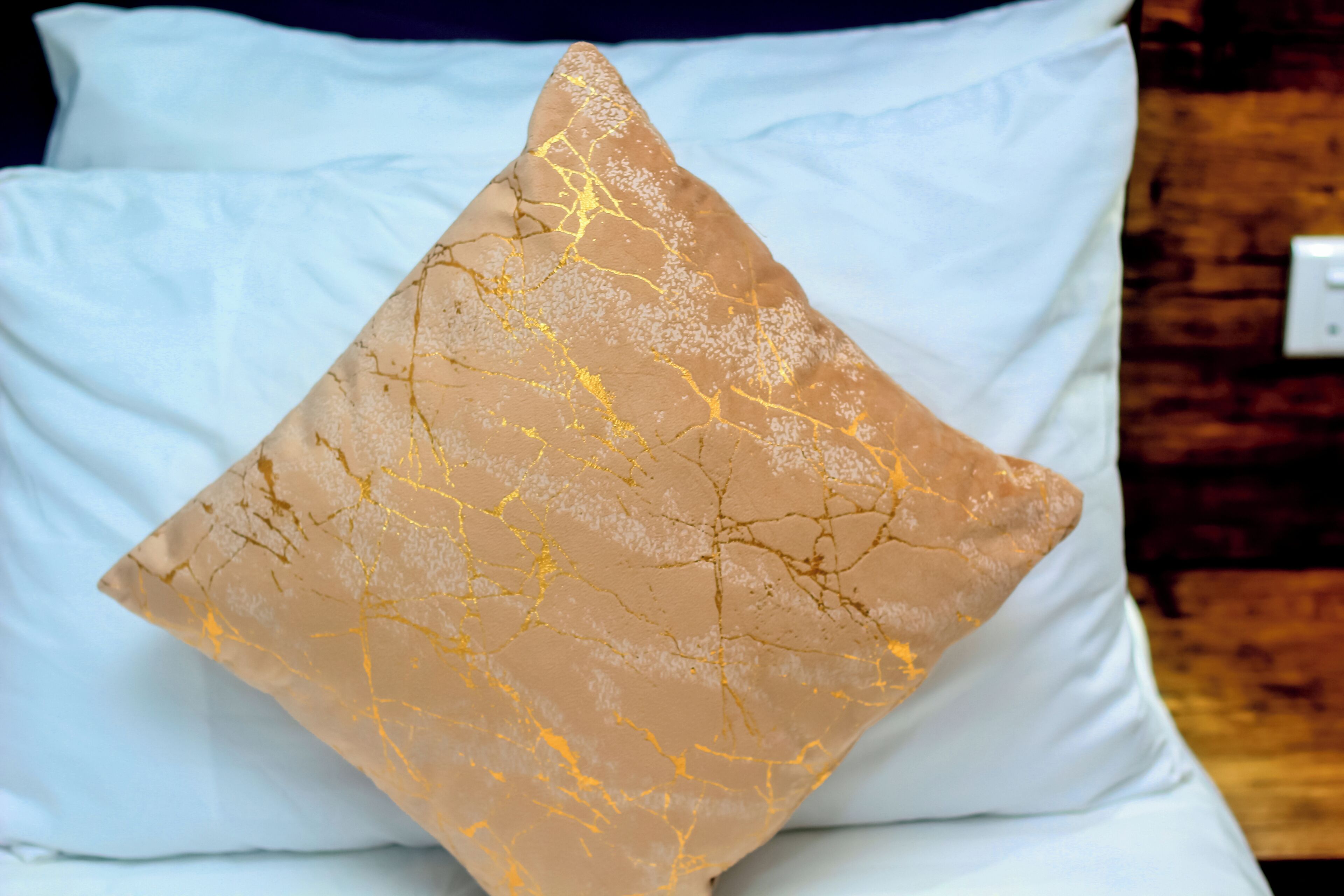 A bed with a white sheet and a single decorative pillow with a gold pattern.