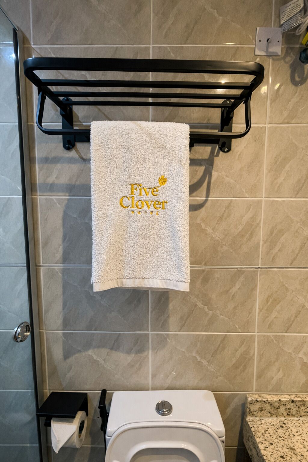 A bathroom with a white toilet, a towel rack with a towel, and a marble-tiled wall.
