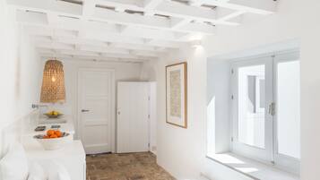 Un interior luminoso y blanco con suelo de piedra, un banco blanco, una lámpara de mimbre y un cuadro en la pared.