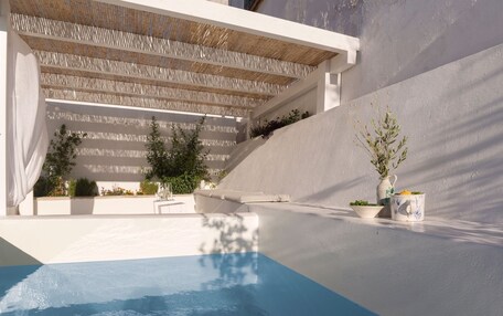 A modern pool area with a clear blue pool, white walls, and a pergola with a woven roof.