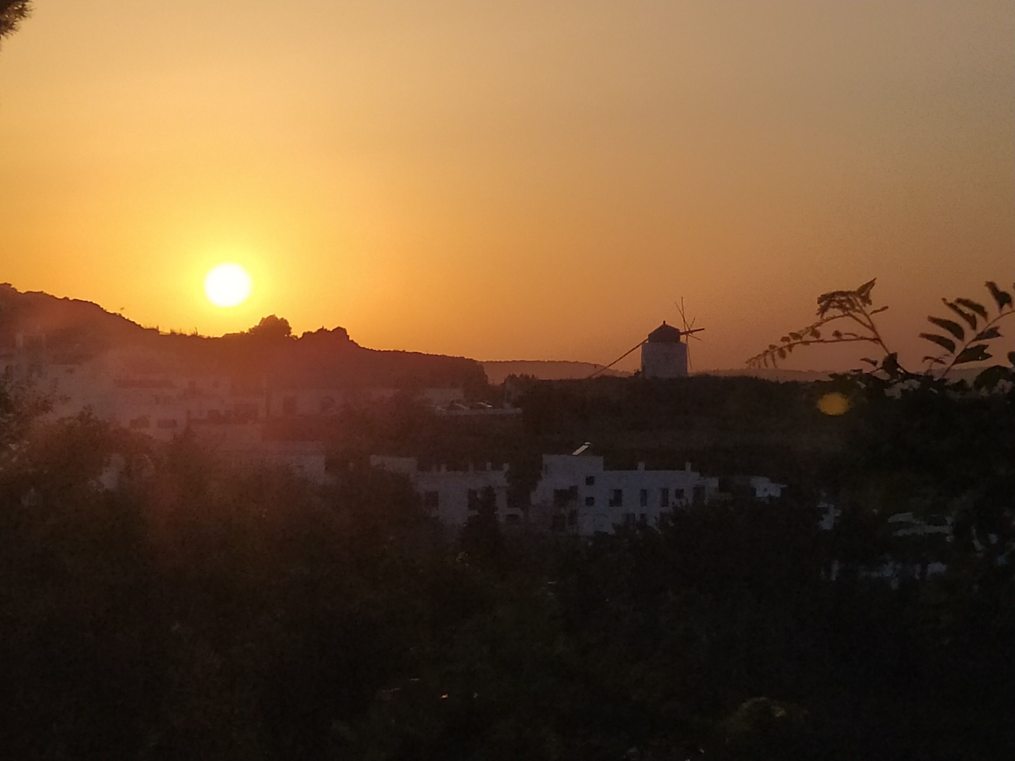 A sunset over a town with buildings and a windmill.