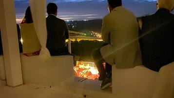 Un grupo de personas sentadas en un banco blanco con vistas a un paisaje urbano al anochecer.