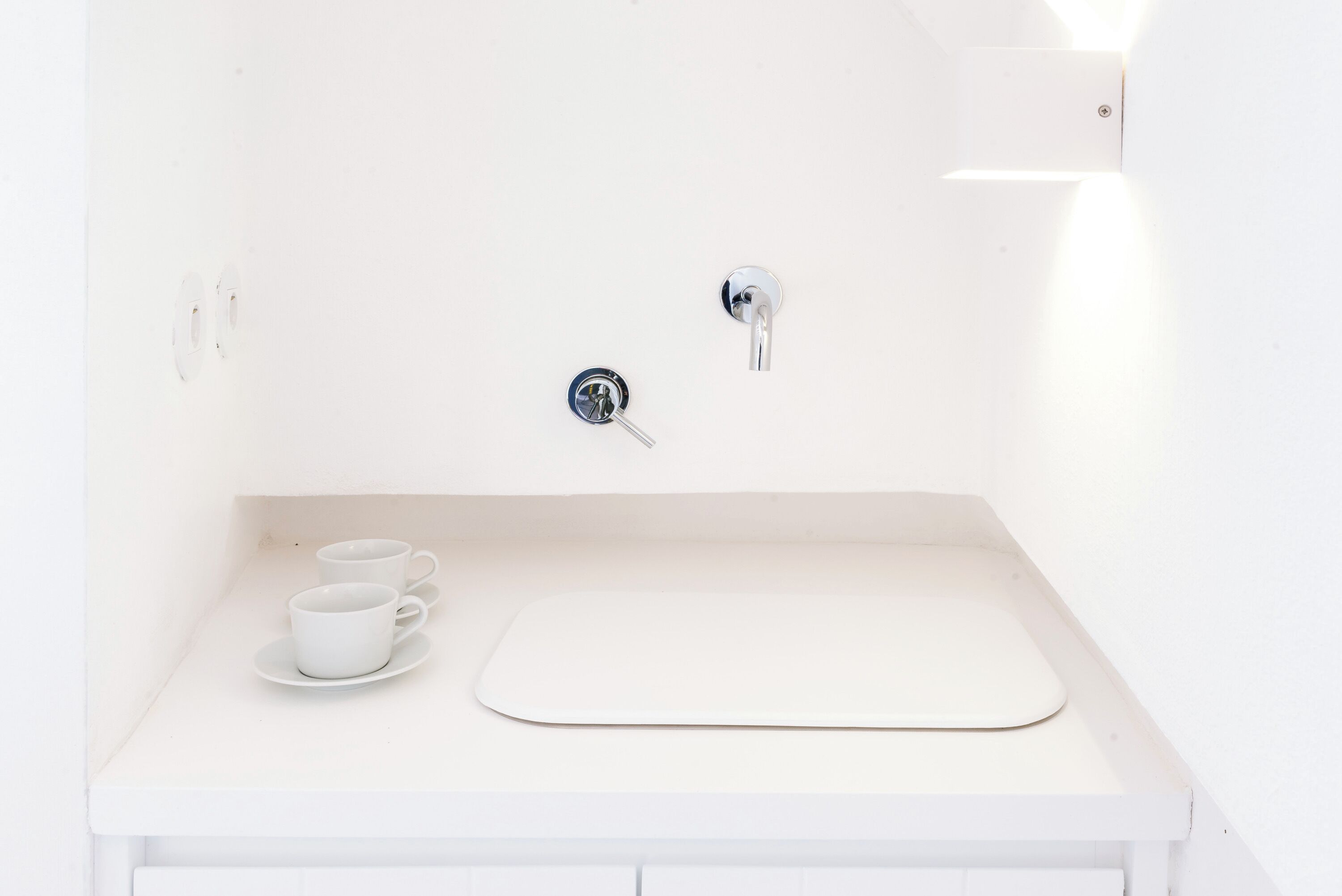 Un baño blanco con un lavamanos, dos grifos y dos vasos sobre la encimera.