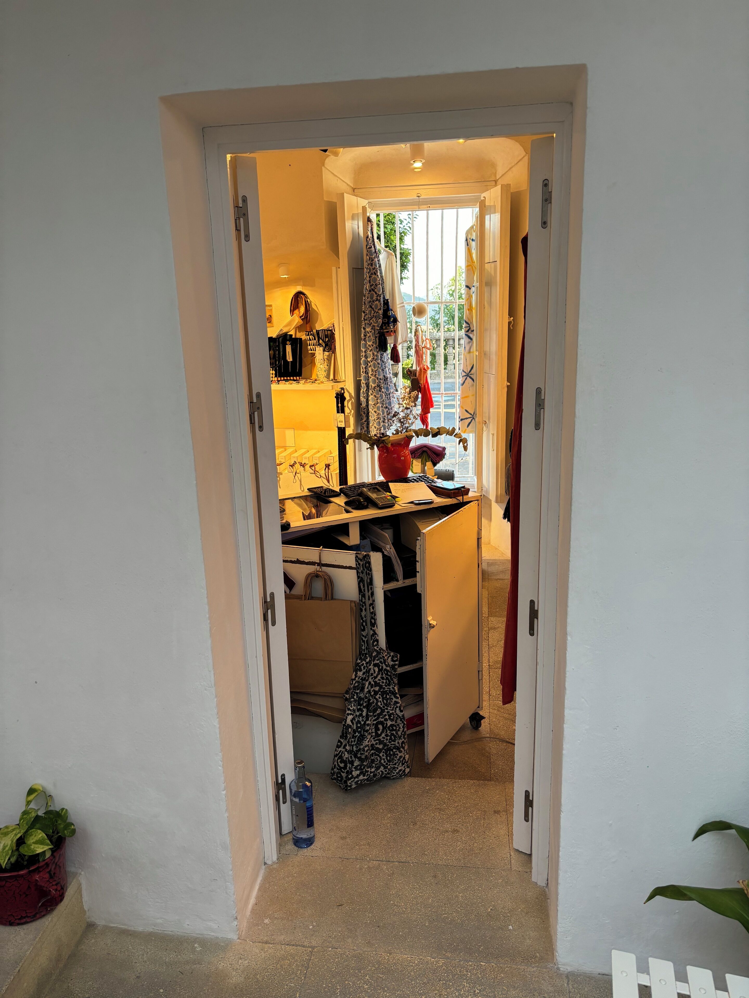 A narrow hallway with a door leading to a room containing a desk, chair, and various personal items.