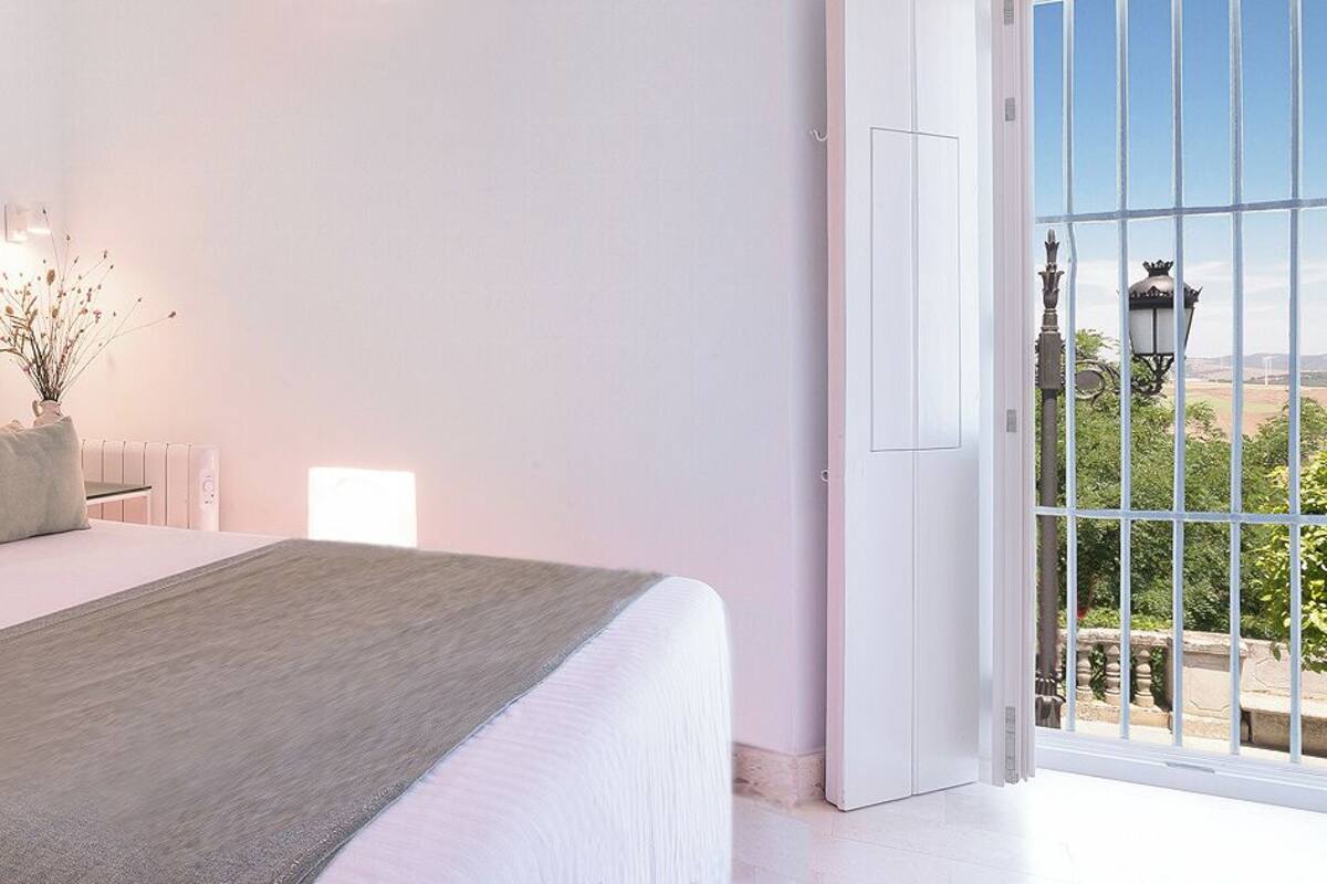 Une chambre à coucher avec un lit, des oreillers, une table de chevet, un vase avec des fleurs et une fenêtre donnant sur un beau paysage.