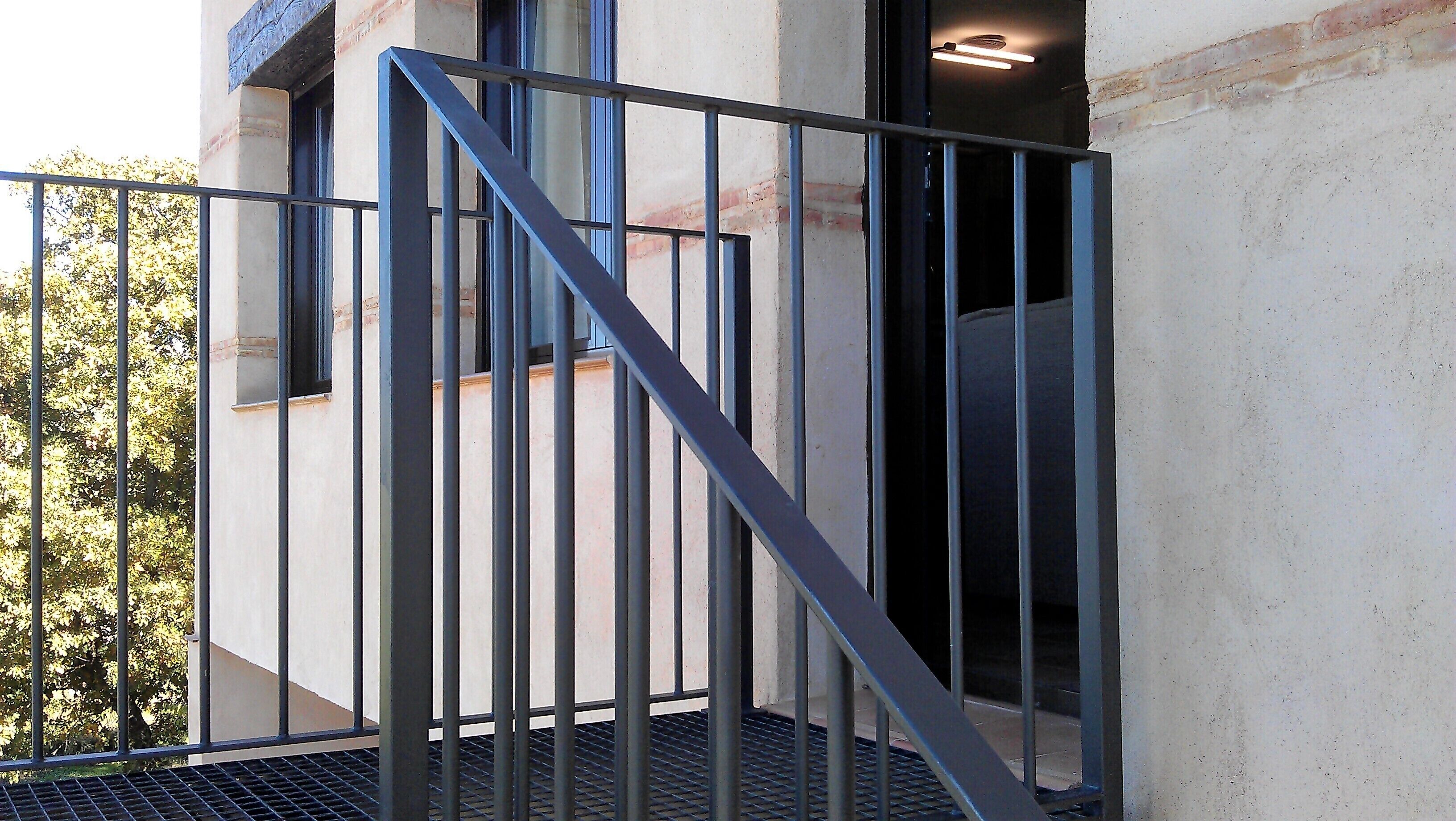 Eine Metalltreppe mit Handlauf führt zu einer Tür, einem Fenster und einer Wand mit strukturierter Oberfläche.
