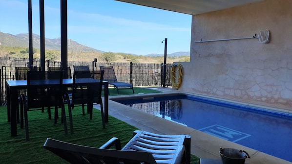 An outdoor pool area with a table and chairs, a hose reel, and a view of distant mountains.