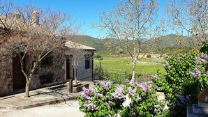 A stone building with a balcony, a bench, and a view of a green field and mountains. - House with private pool in Cabañeros National Park (Navas de Estena)