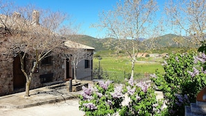 A stone building with a balcony, a bench, and a view of a green field and mountains.
