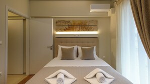 A hotel room with a large bed, a headboard with a light fixture, and two towels on the bed. - Blue Ark Harmony Residence (Nea Smirni)