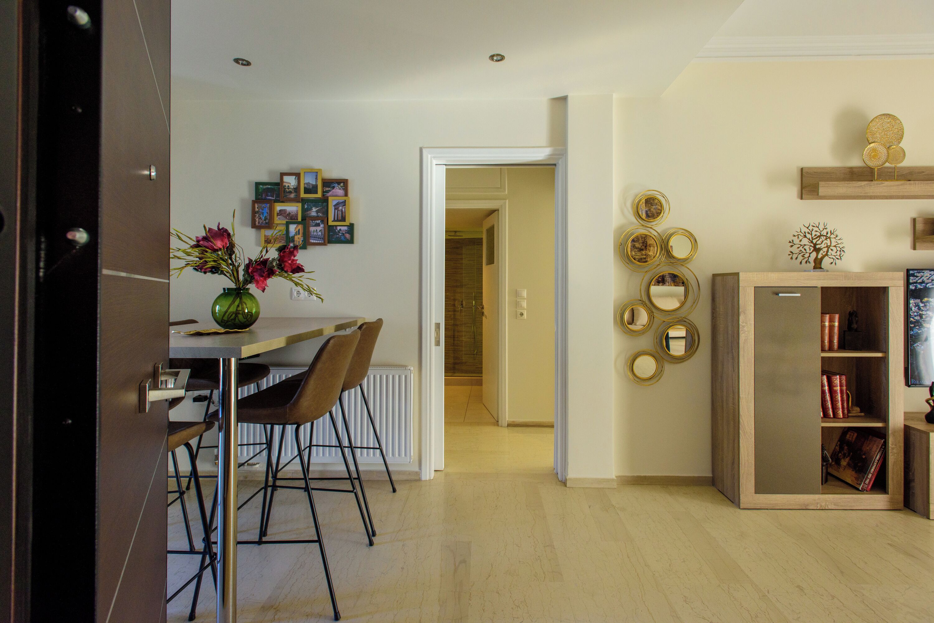 A dining area with a table and chairs, a vase with flowers, and a bookshelf with books and decorative items.