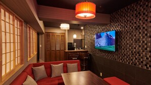Un interior moderno con una mesa de comedor de madera, asientos con cojines rojos, una zona de cocina y un televisor fijado en una pared con textura.