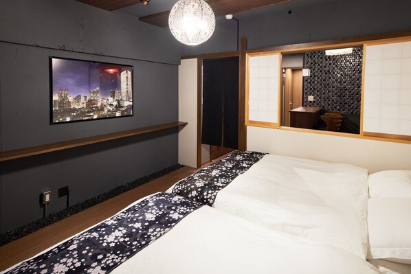 A modern hotel room with a cityscape view, a large bed with floral bedding, a wooden shelf, and a traditional Japanese-style partition. - Kumihimo no ma (Shibuya-ku)
