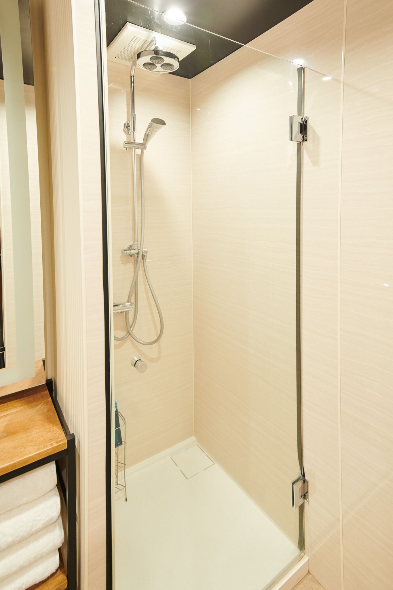 Eine moderne Dusche mit Glastür, Handtuchhalter und Holzablage.