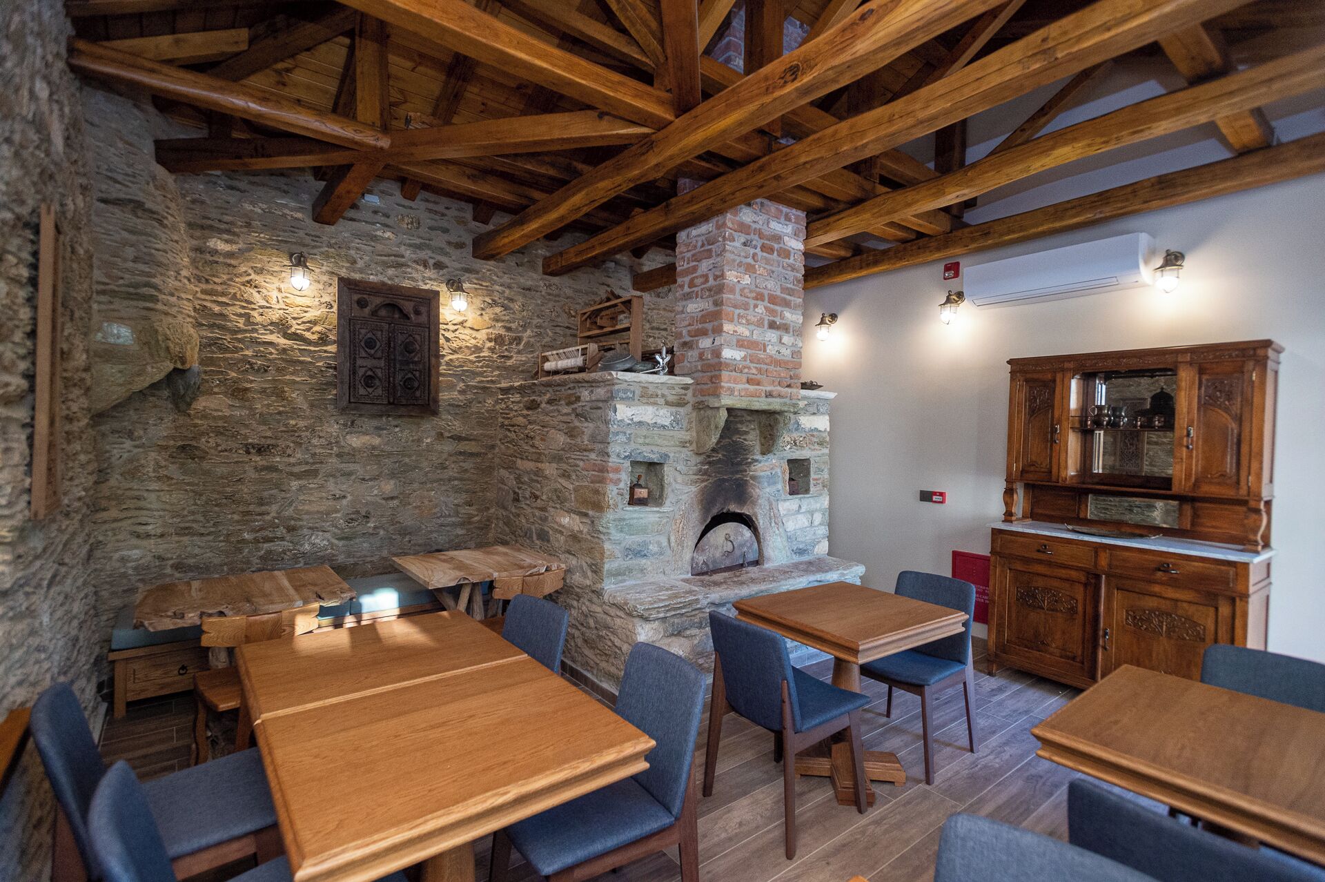 Ein rustikales Interieur mit Steinwänden, Holzbalken, einem Kamin aus Ziegeln und Holzmöbeln.