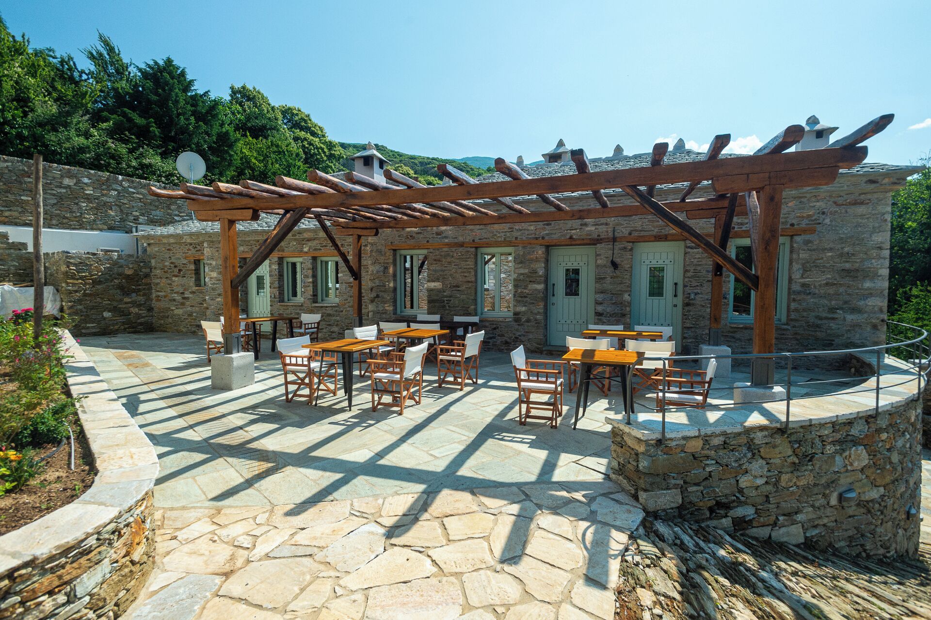 An outdoor patio area with stone flooring and wooden tables and chairs.