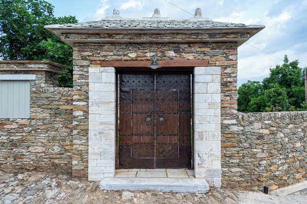 Ein Steinhaus mit einer großen Holztür, einer kleinen Veranda und einer Steinmauer.