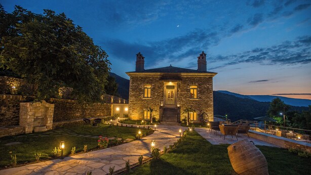 A stone house with a well-lit entrance, a stone pathway, and a view of the mountains in the background. - Nostos Country House (Zagora-Mouresi)
