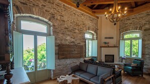 A rustic room with stone walls, wooden furniture, and large windows. - Nostos Country House (Zagora-Mouresi)