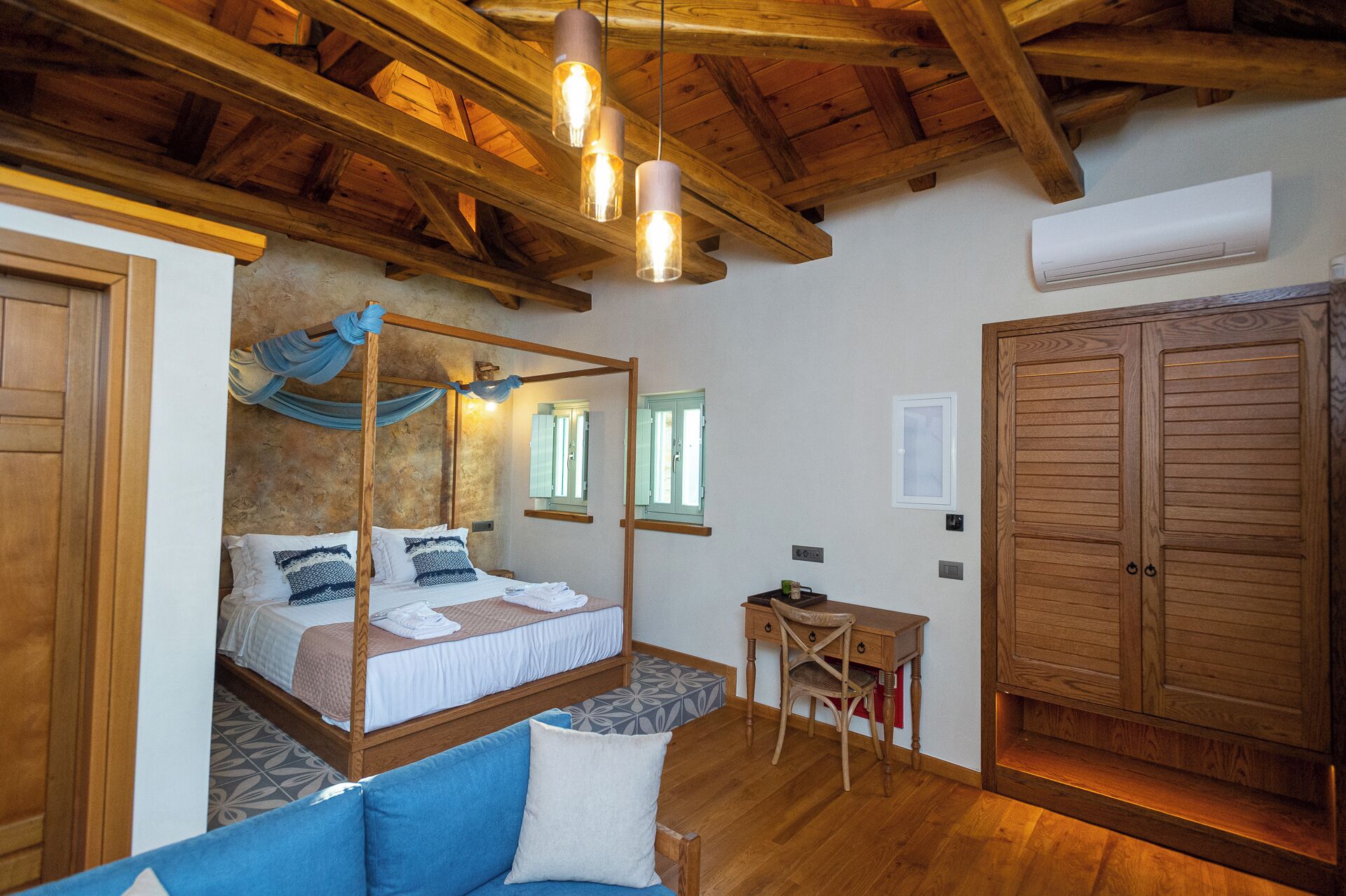 Ein Schlafzimmer mit einem Himmelbett, Holzbalken an der Decke, einem kleinen Schreibtisch und einem Kleiderschrank.