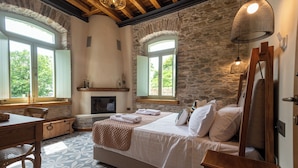 A bedroom with a large bed, a wooden desk, a fireplace, and stone walls. - Nostos Country House (Zagora-Mouresi)