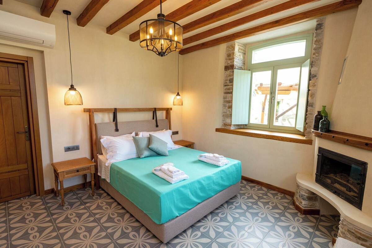 Une chambre à coucher avec un lit, des tables de chevet, une cheminée et une fenêtre donnant sur un beau paysage.