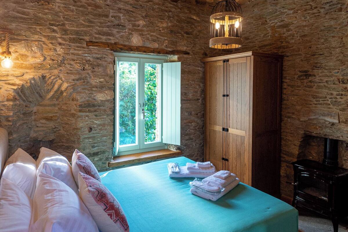 Une pièce chaleureuse avec un lit, un mur en pierre, une fenêtre et une cheminée.