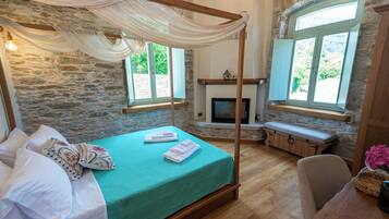 A room with a four-poster bed, a stone wall, a fireplace, and large windows.