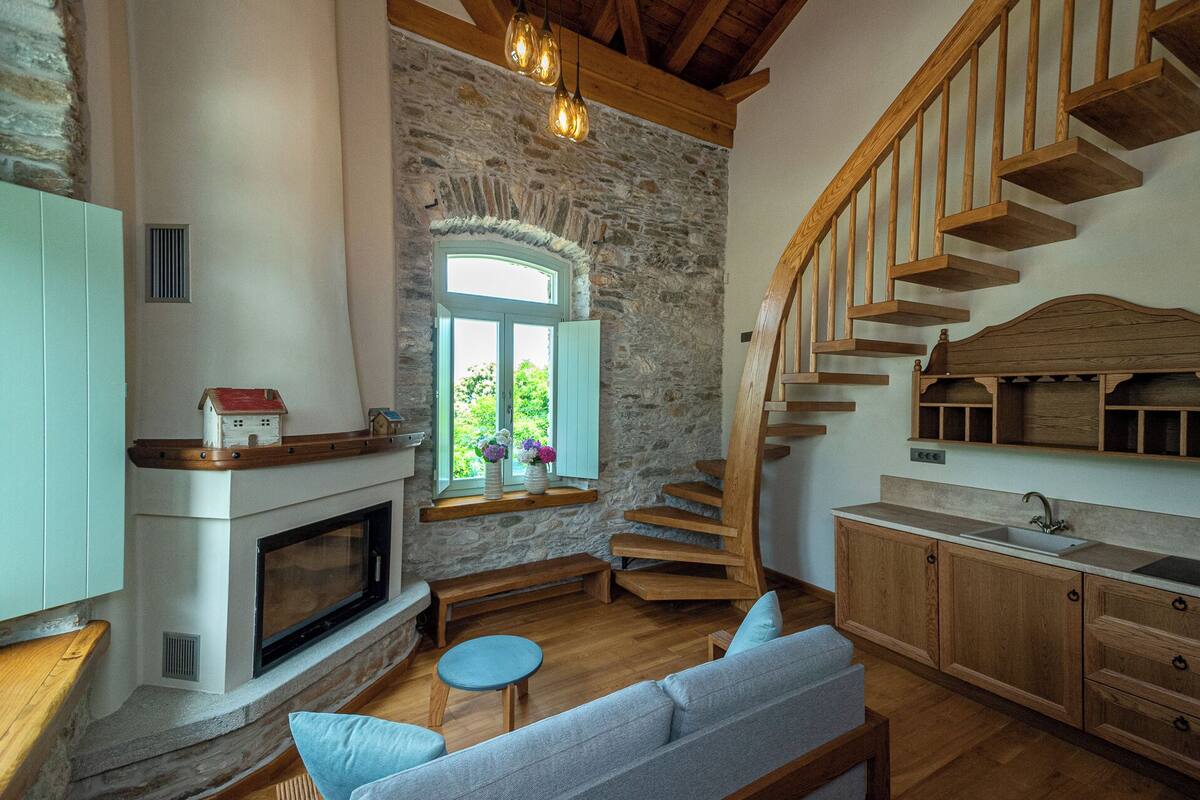 Un intérieur chaleureux avec un mur en pierre, un escalier en bois, une cheminée et un canapé.