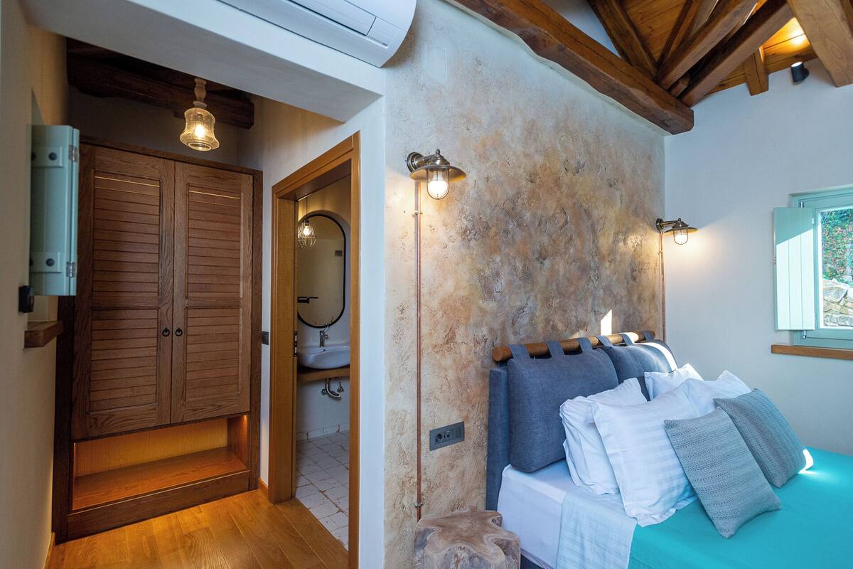 Une chambre à coucher avec un lit, une armoire en bois et une salle de bain équipée d’un miroir et d’un lavabo.