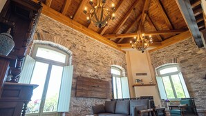 A rustic interior with exposed wooden beams, stone walls, and a stone fireplace. There is a wooden sofa and two chairs in the seating area. - Nostos Country House (Zagora-Mouresi)