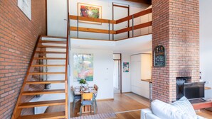 Eine moderne Loft-Wohnung mit einer Holztreppe, einem Essbereich, einem Wohnzimmer mit einer Couch und einem Kamin aus Ziegelsteinen.