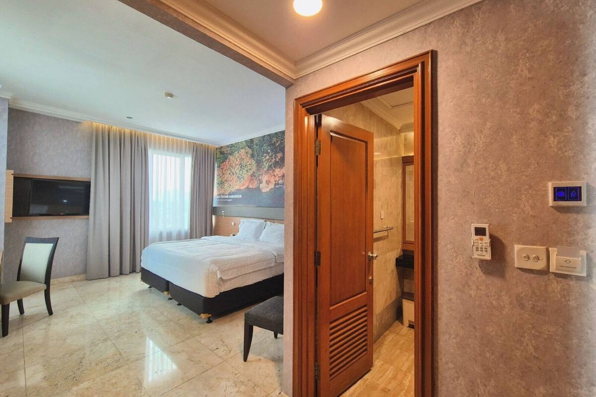 Une chambre d’hôtel équipée d’un lit, d’un bureau, d’une chaise, d’une télévision, d’une douche et d’une porte dotée d’un panneau de commande.
