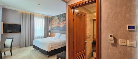 A hotel room with a bed, a desk, a chair, a television, a shower, and a door with a control panel.