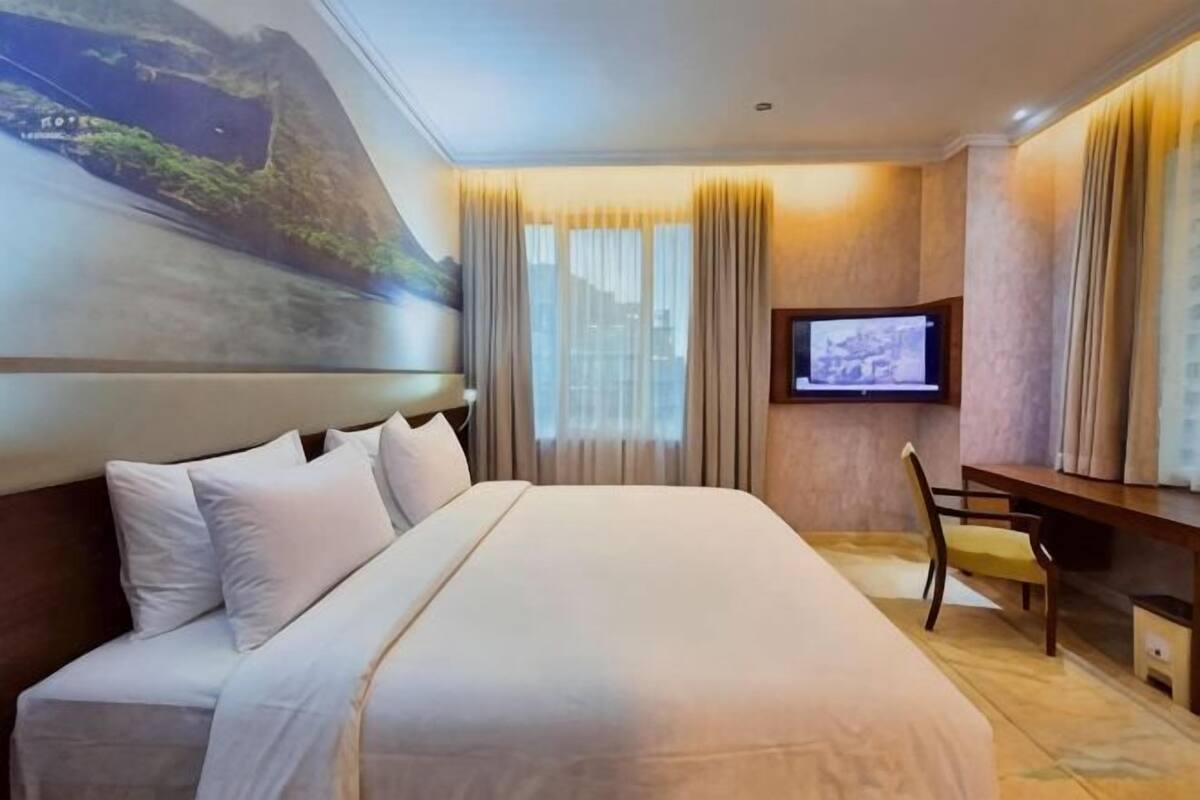 Une chambre d’hôtel avec un grand lit, un bureau, une télévision et un tableau au mur.