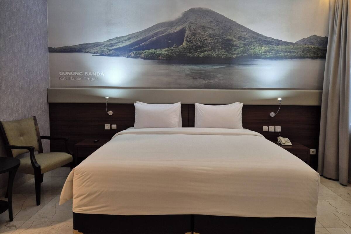 Une chambre d’hôtel avec un grand lit, une chaise, un téléphone et une œuvre d’art fixée au mur représentant une montagne et un lac.