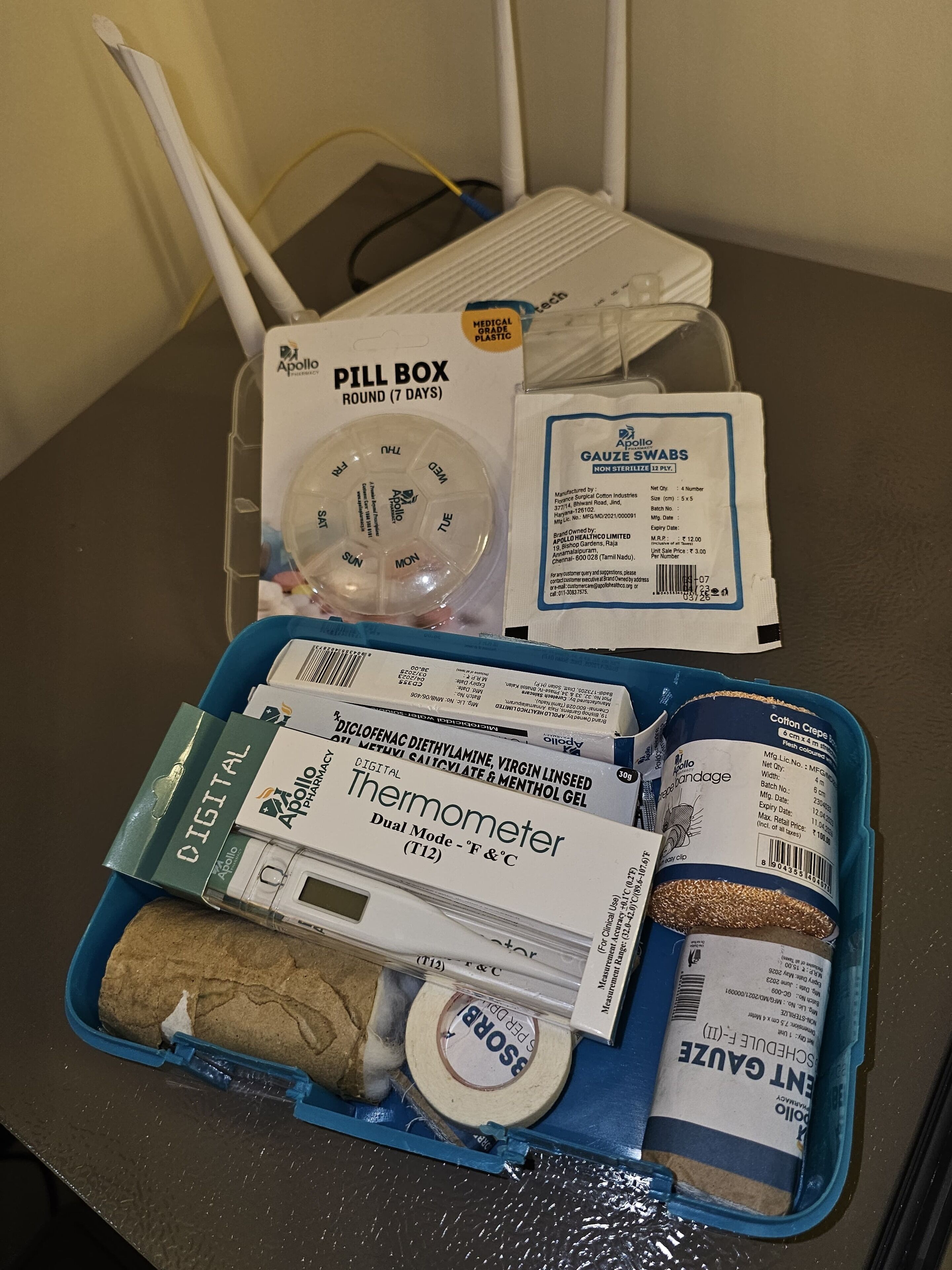 A medical kit with a pill organizer, thermometer, cotton swabs, and gauze.