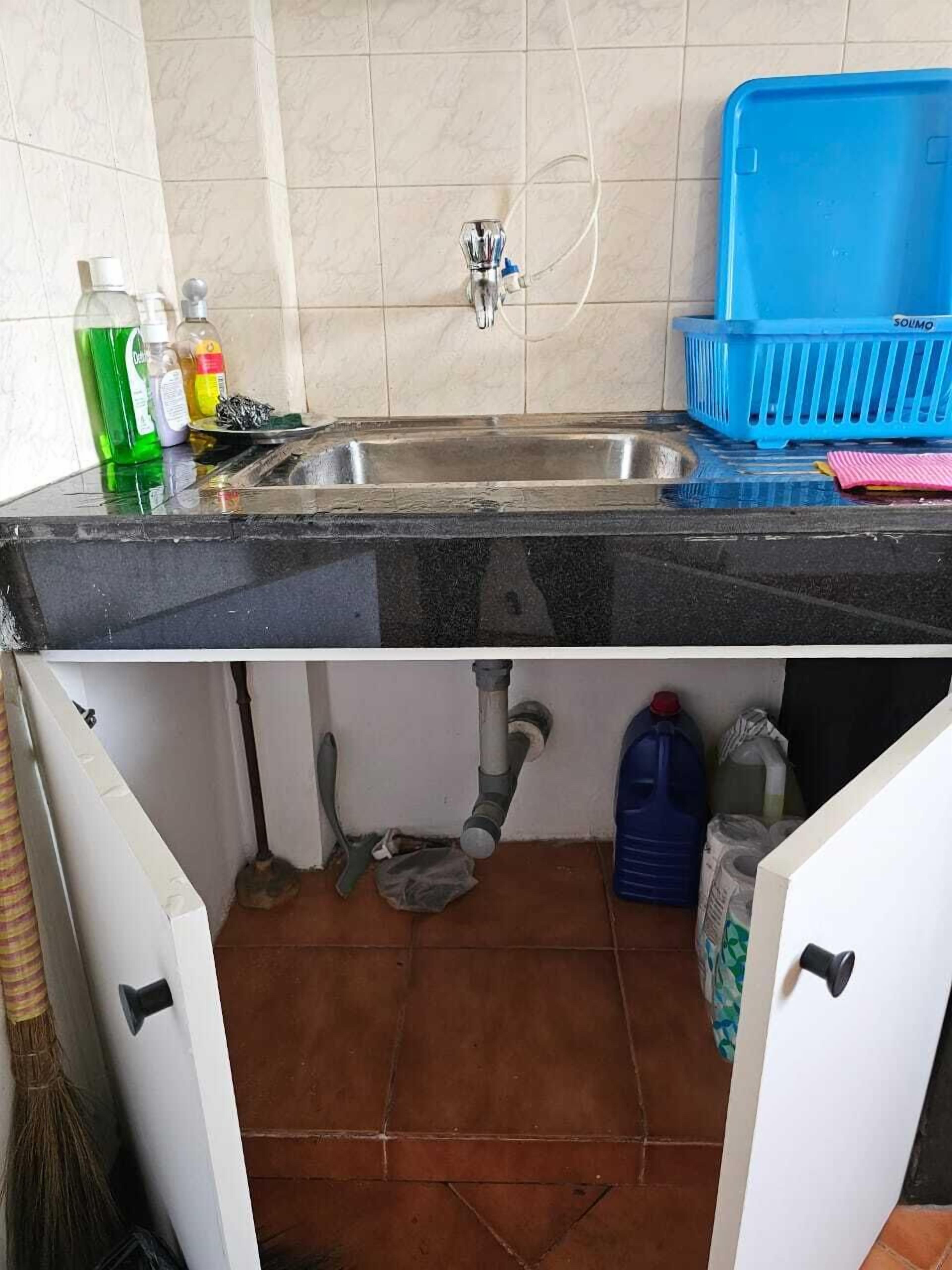 Una cocina con un lavamanos, una escoba y productos de limpieza.