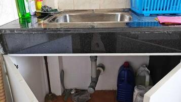 Una cocina con un lavamanos, una escoba y productos de limpieza.