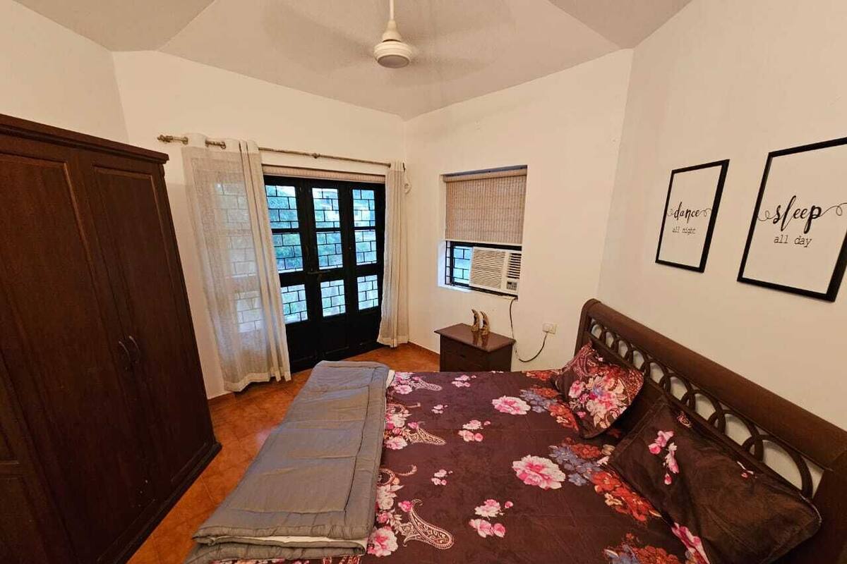 A bedroom with a bed, a wardrobe, a window with curtains, and a wall with framed text.