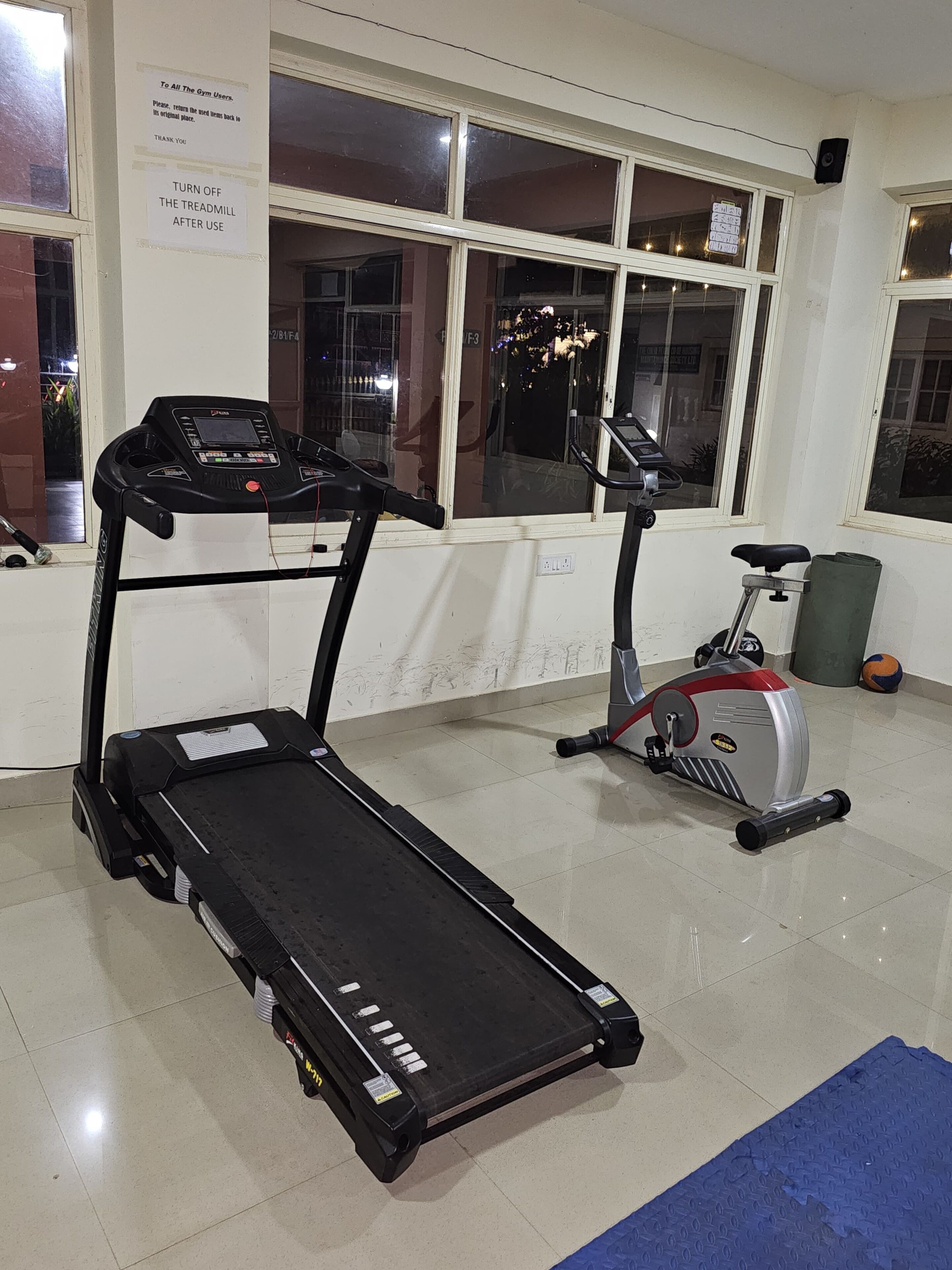 A gym with two treadmills, a stationary bike, and a blue mat on the floor.
