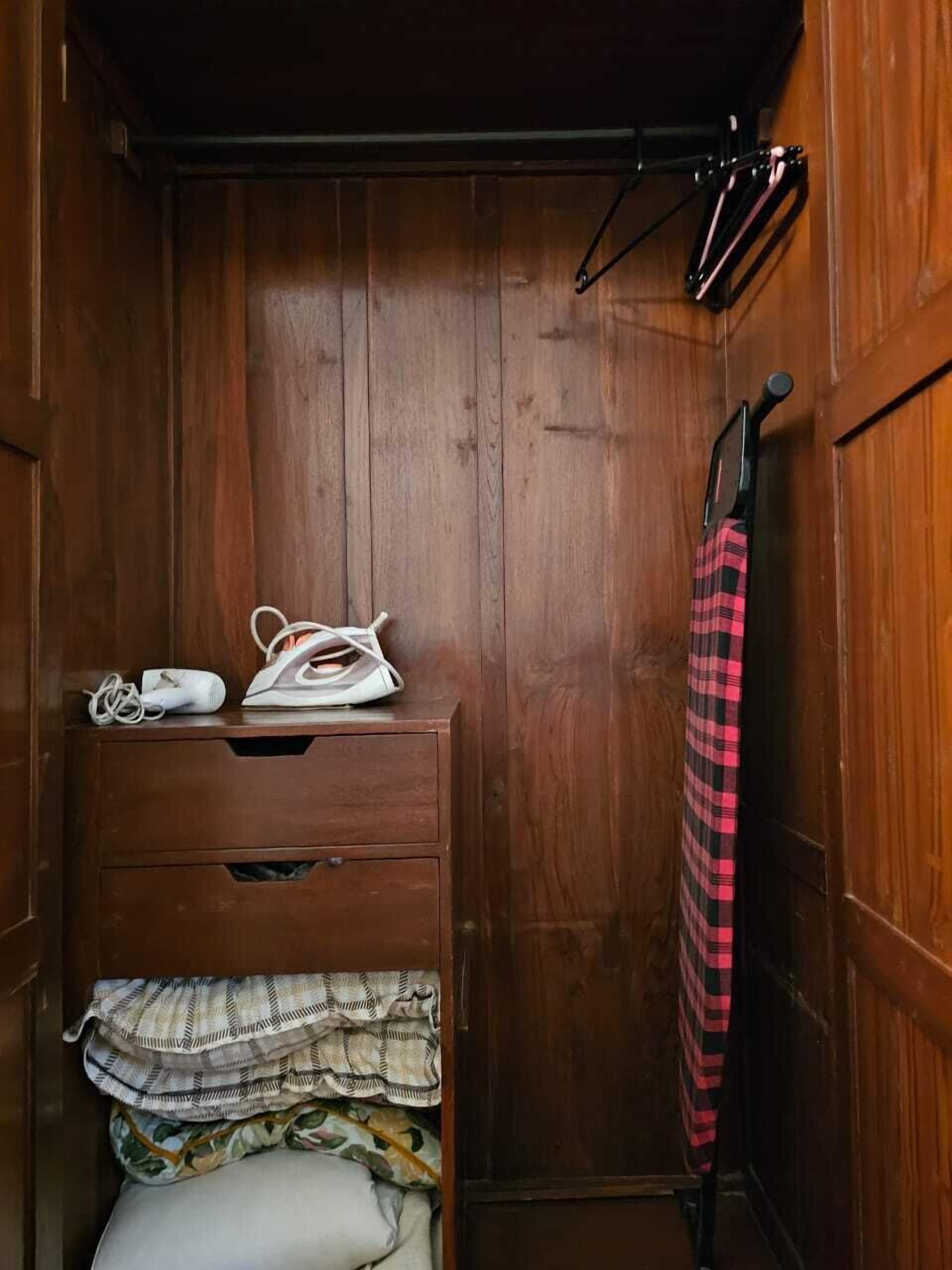 A wooden wardrobe with a hanging rack, a folded bed, and a red plaid towel.
