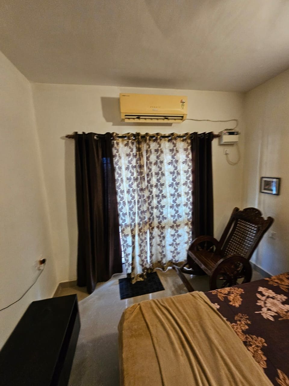 Une pièce comprenant un lit, une chaise, un bureau, un appareil de climatisation et un rideau.