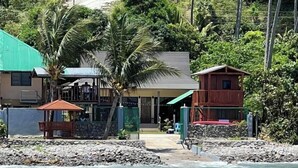 Una proprietà costiera con piscina, un piccolo edificio e vista su una collina con palme.
