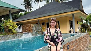 Una persona seduta a bordo piscina, con una casa sullo sfondo.